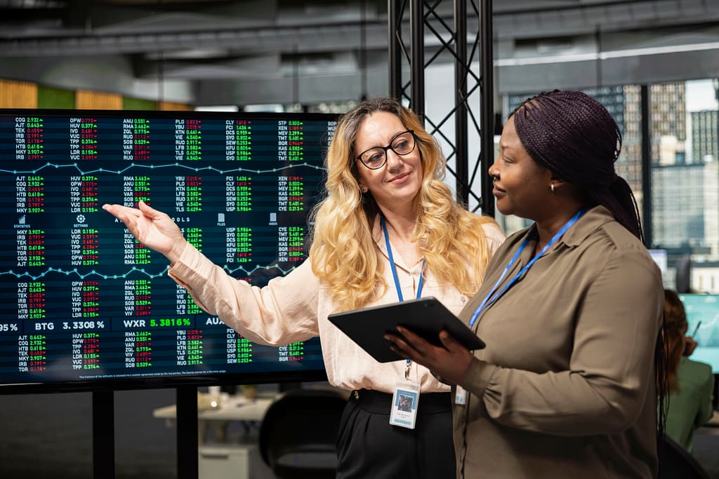 Diverse businesswomen working side by side to review data on TV monitor
